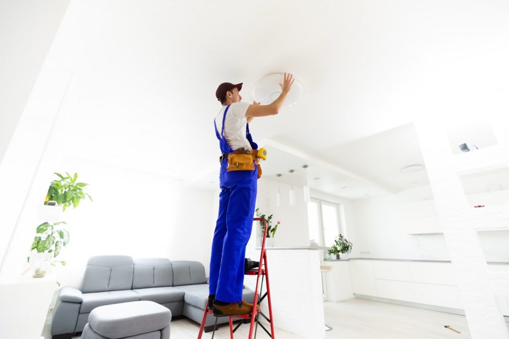 Electrician at work. Service for the repair of electrical wiring and replacement of ceiling lamps. A builder is installing a loft-style wooden ceiling. Rent-a-gent helps with the housework.