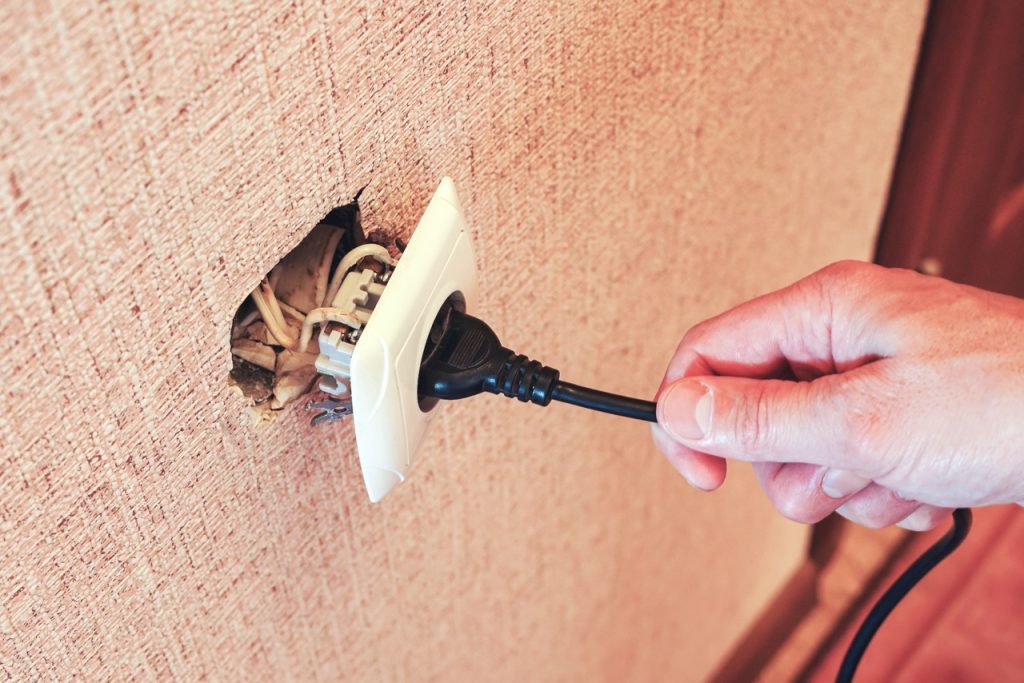 Unsafe use of a damaged two-prong electrical outlet, highlighting the need for outlet replacement services by Dustmen Electric.